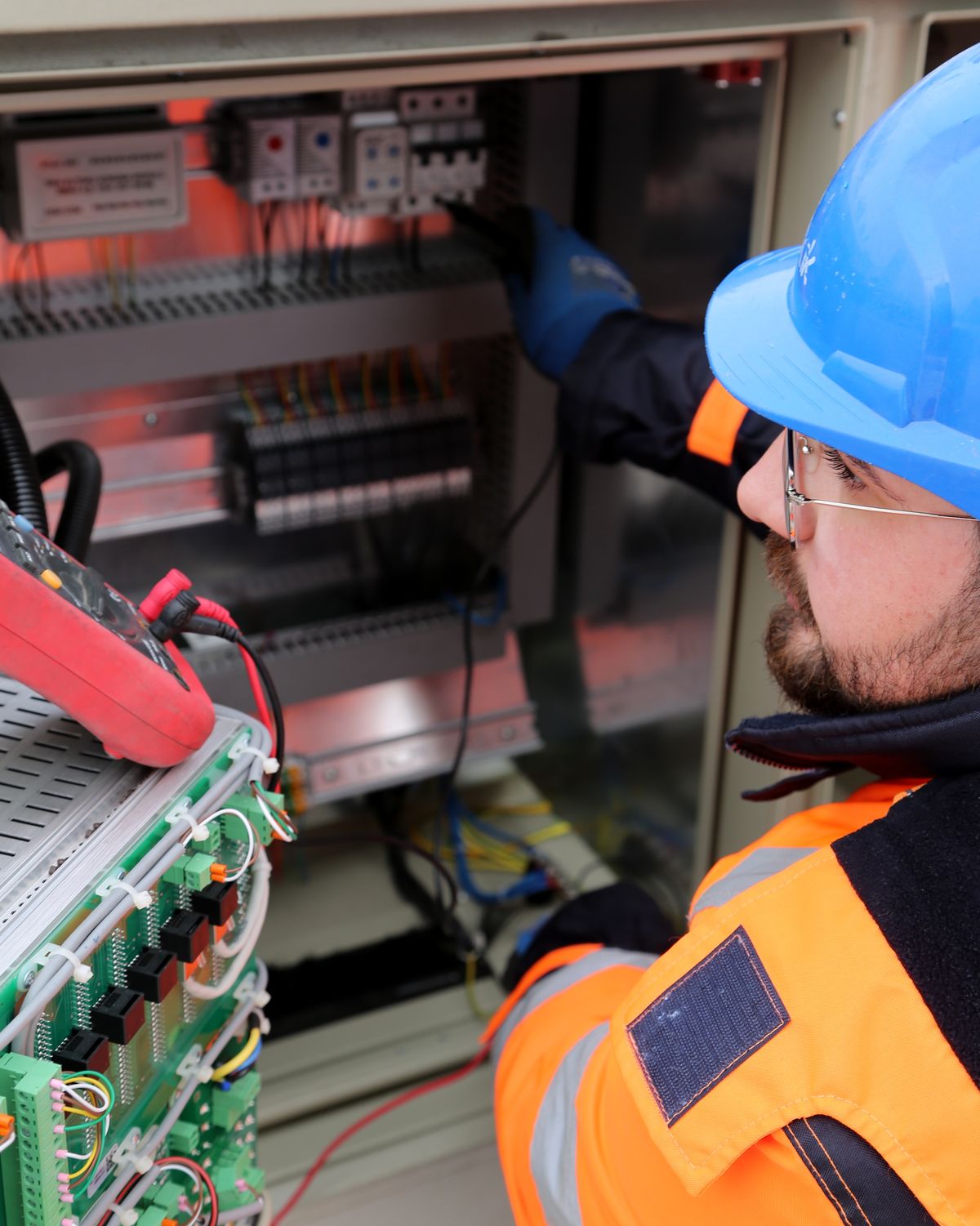 Electrician in a hard hat and high-visibility workwear inspecting an electrical panel